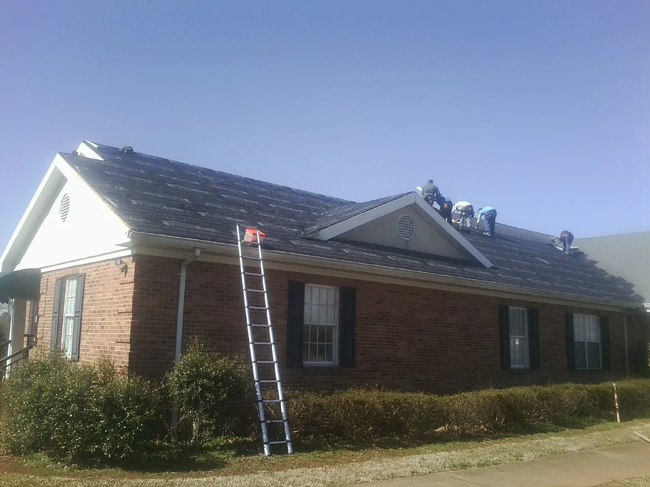 Crew tearing shingles off a brick ranch roof with a ladder set — Metal Roof Repair work by our crew in Columbia Station