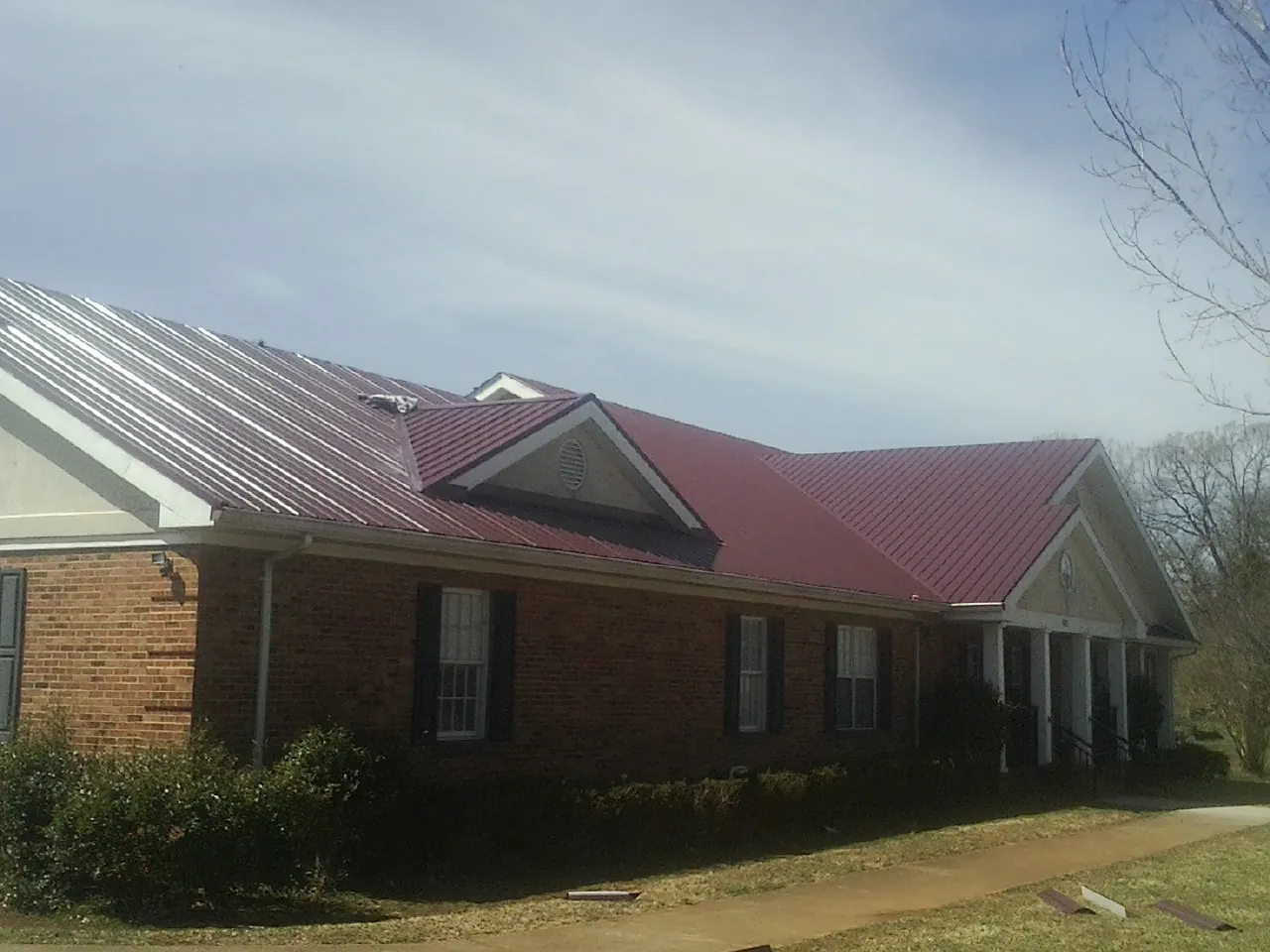Red metal roof with gabled entries on a long brick building, from a Hail Damage Roof Repair job in Columbia Station