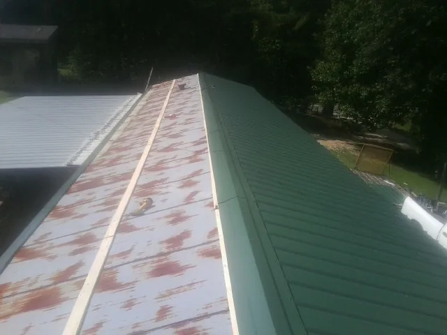 Old rusted panels beside newly installed green metal roofing — Wind Damage Roof Repair by Roofing Brothers in Columbia Station