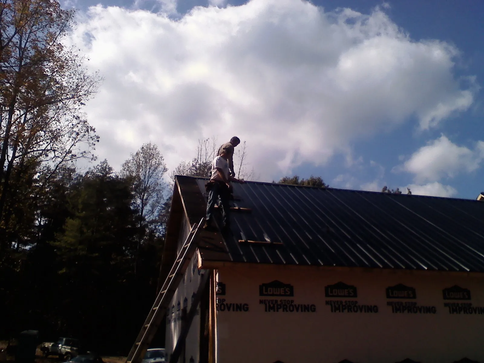 Roofer fastening dark metal panels high against a cloudy sky, from a Roof Inspection job in Columbia Station