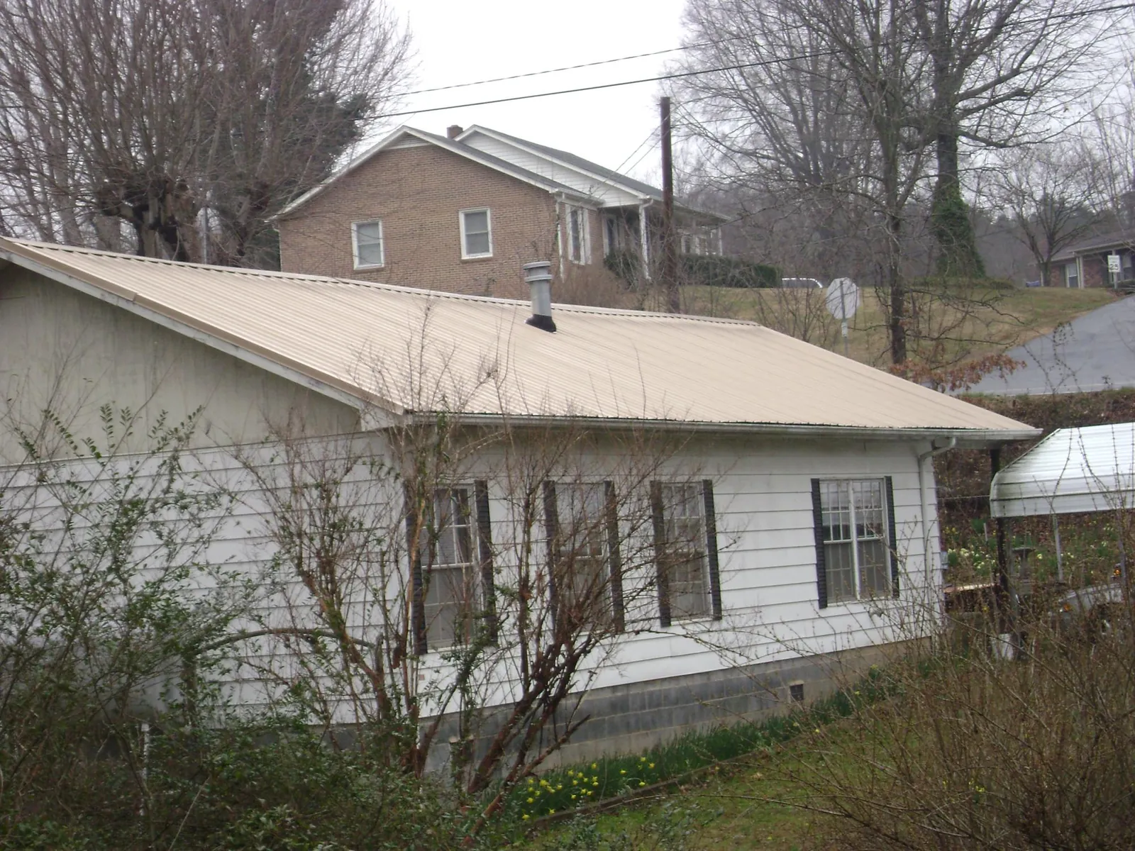 Tan metal roof on a white sided house set into a hillside — Commercial Roofing by Roofing Brothers in Columbia Station