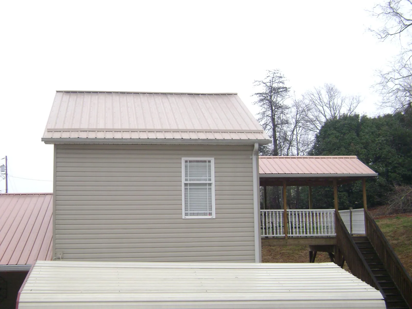 Tan metal roofs on a two story addition and attached porch, from a Roof Replacement job in Columbia Station